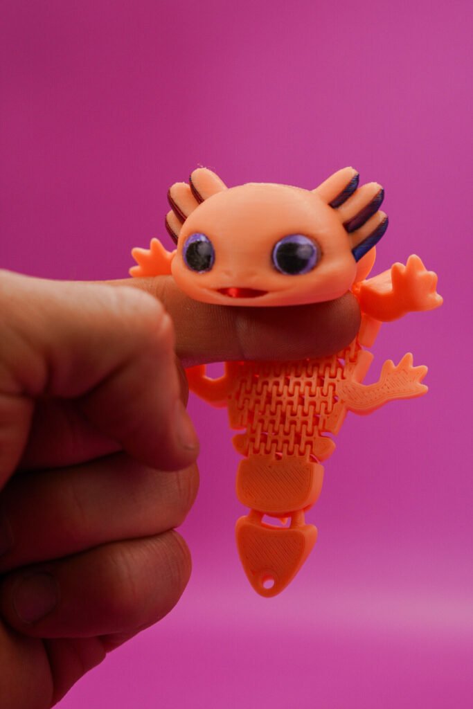 3D printed orange Flexolotl (flexible articulated axolotl figurine) held in hand, full body view