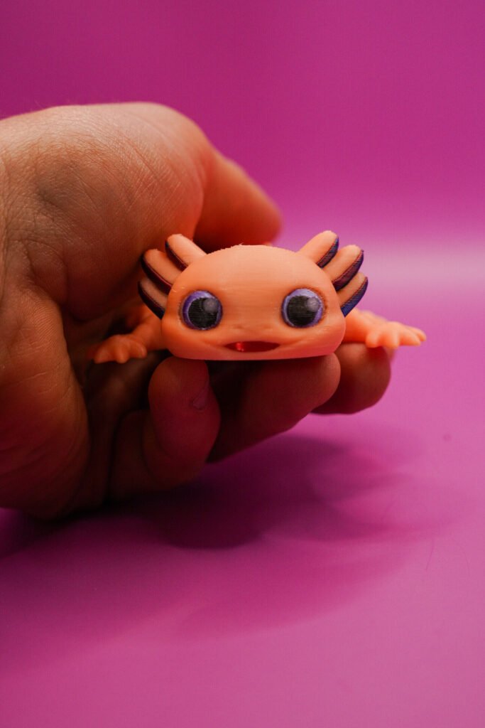 3D printed orange Flexolotl (flexible articulated axolotl figurine) held in hand, close-up